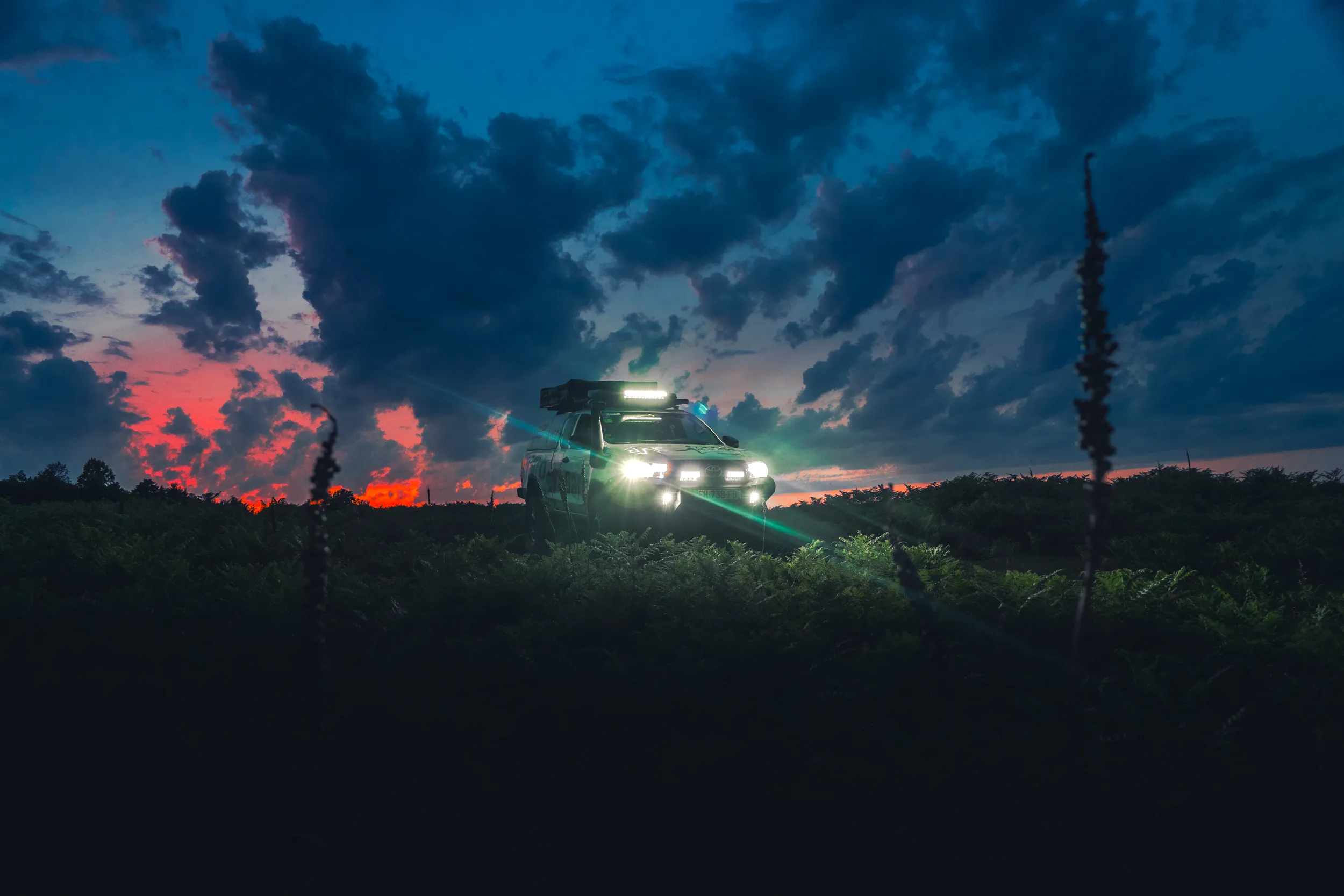 4x4 aux phares allumés dans la campagne au crépuscule, sous un ciel nuageux
