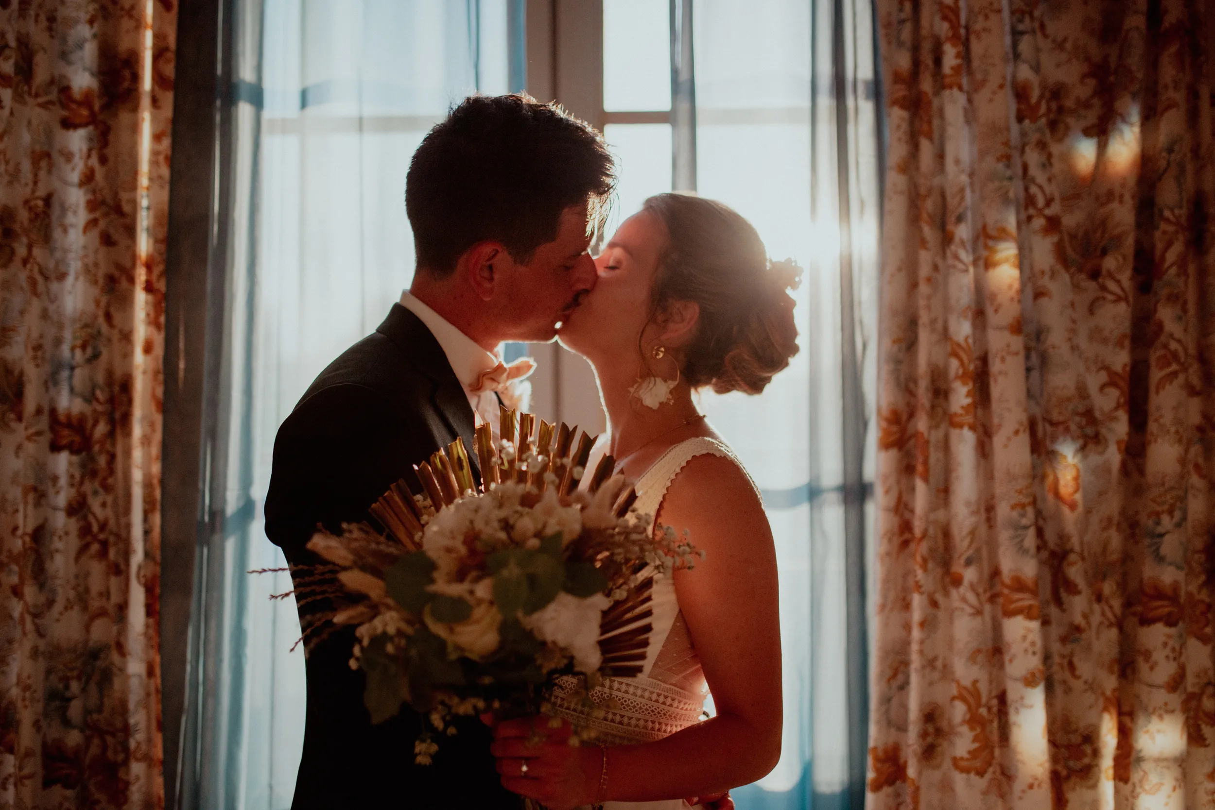 Baiser des mariés en contre-jour devant une fenêtre, lors d'un mariage dans les Landes