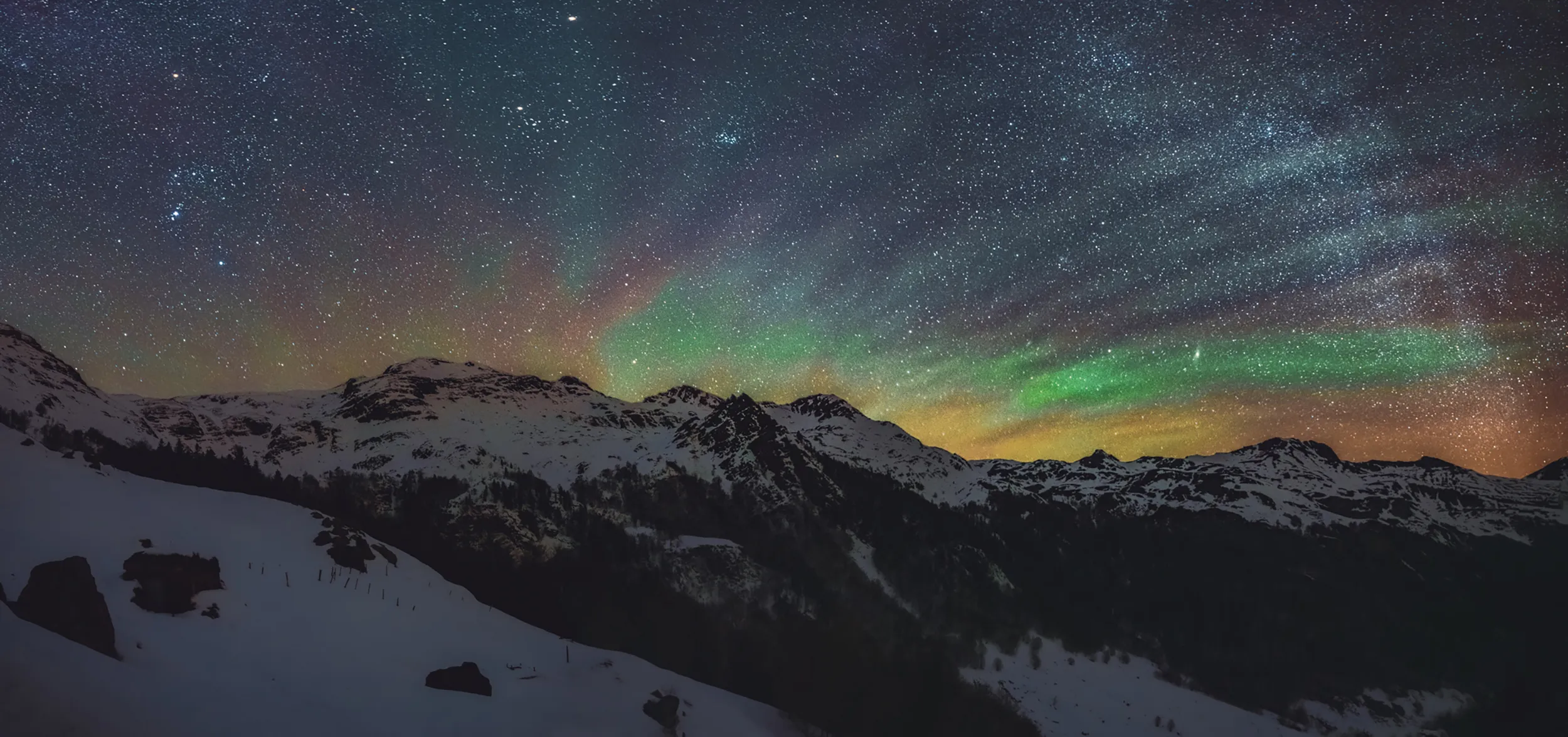 Ciel étoilé zébré de lueurs vertes d'airglow au-dessus de crêtes enneigées des Pyrénées