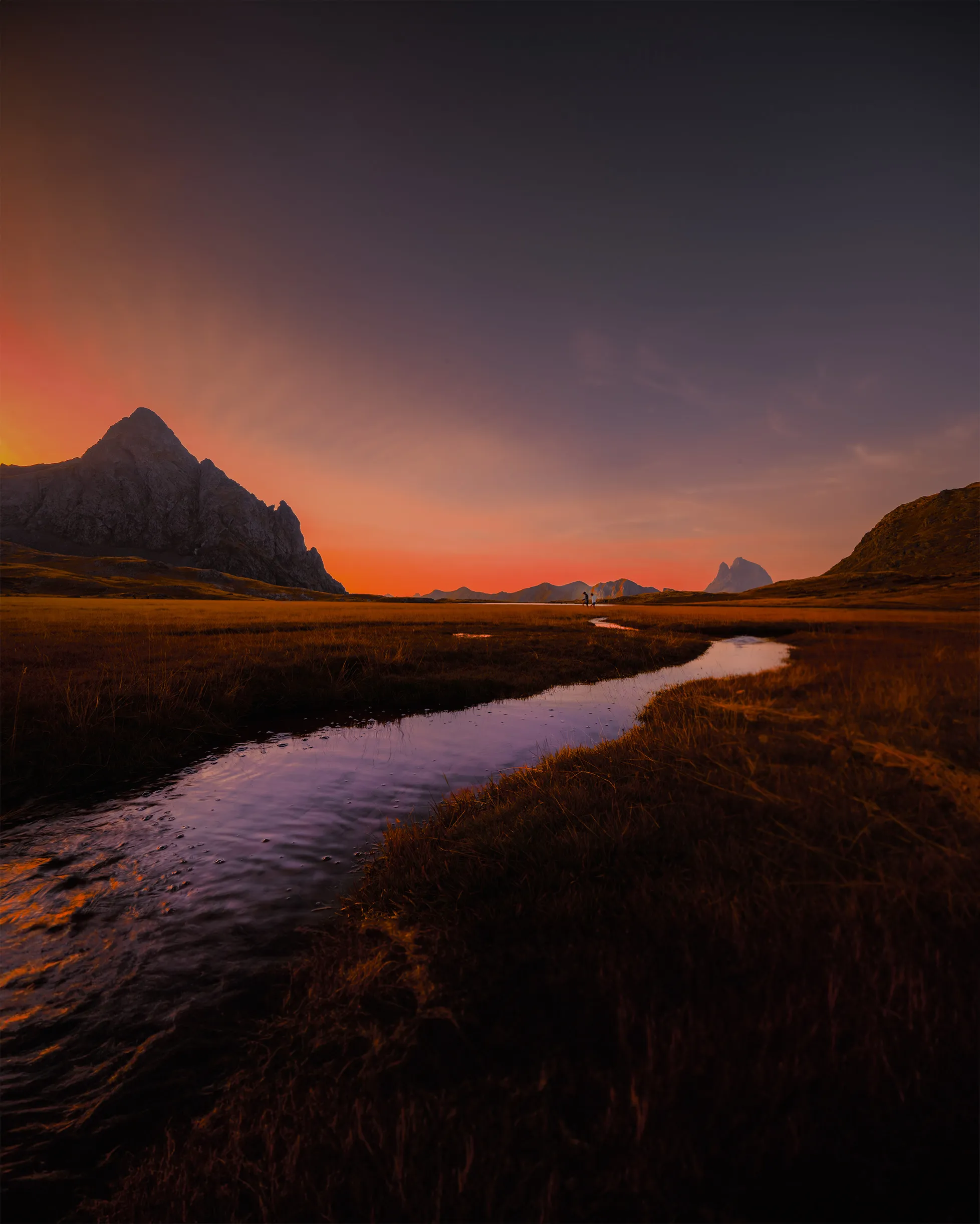 Un ruisseau serpente dans les herbes du plateau d'Anayet au crépuscule, entre le pic d'Anayet et le Midi d'Ossau