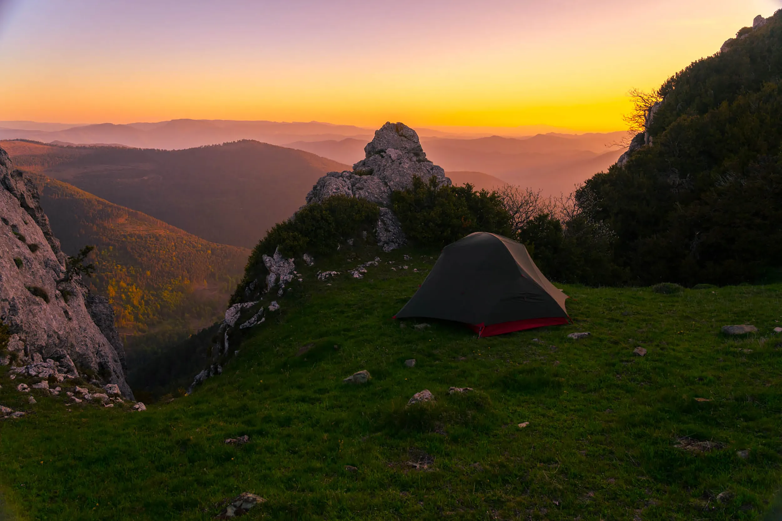 Une tente plantée sur un éperon herbeux face aux collines pyrénéennes, au coucher du soleil