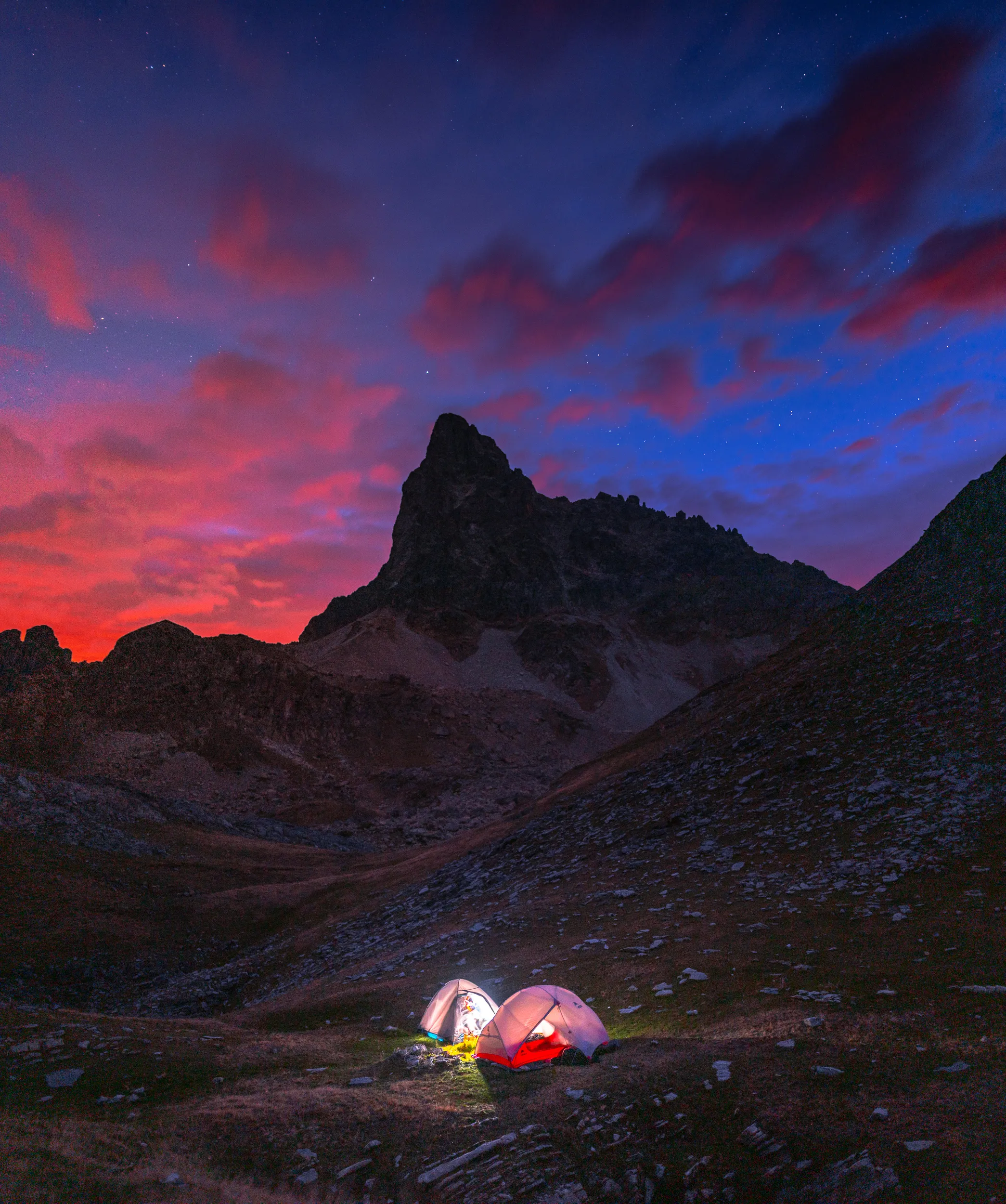 Deux tentes éclairées au pied d'un pic rocheux, sous un ciel rose et bleu au crépuscule, vallée d'Ossau
