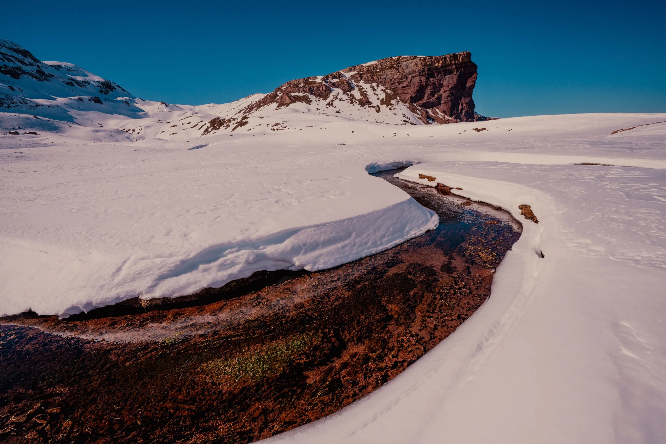 Un ruisseau trace une courbe dans la neige au pied d'un éperon rocheux, au col d'Arrouy