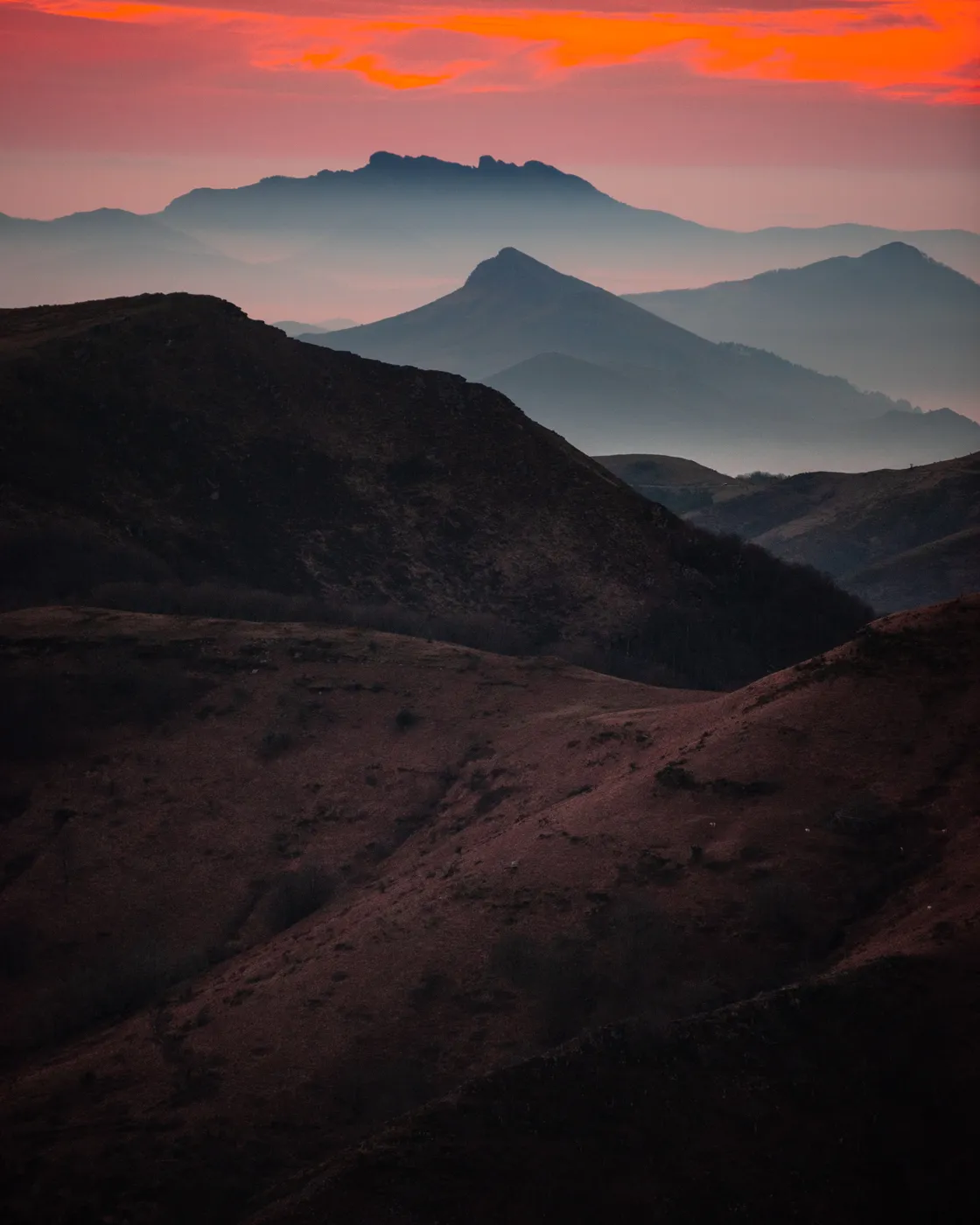 Des crêtes bleutées en plans successifs sous un ciel rouge, vues depuis la crête d'Iparla