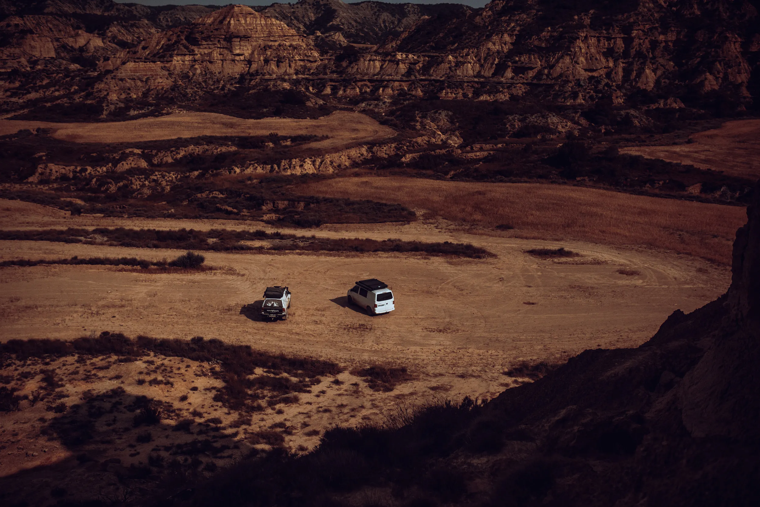 Deux 4x4 isolés dans une vaste plaine désertique bordée de falaises