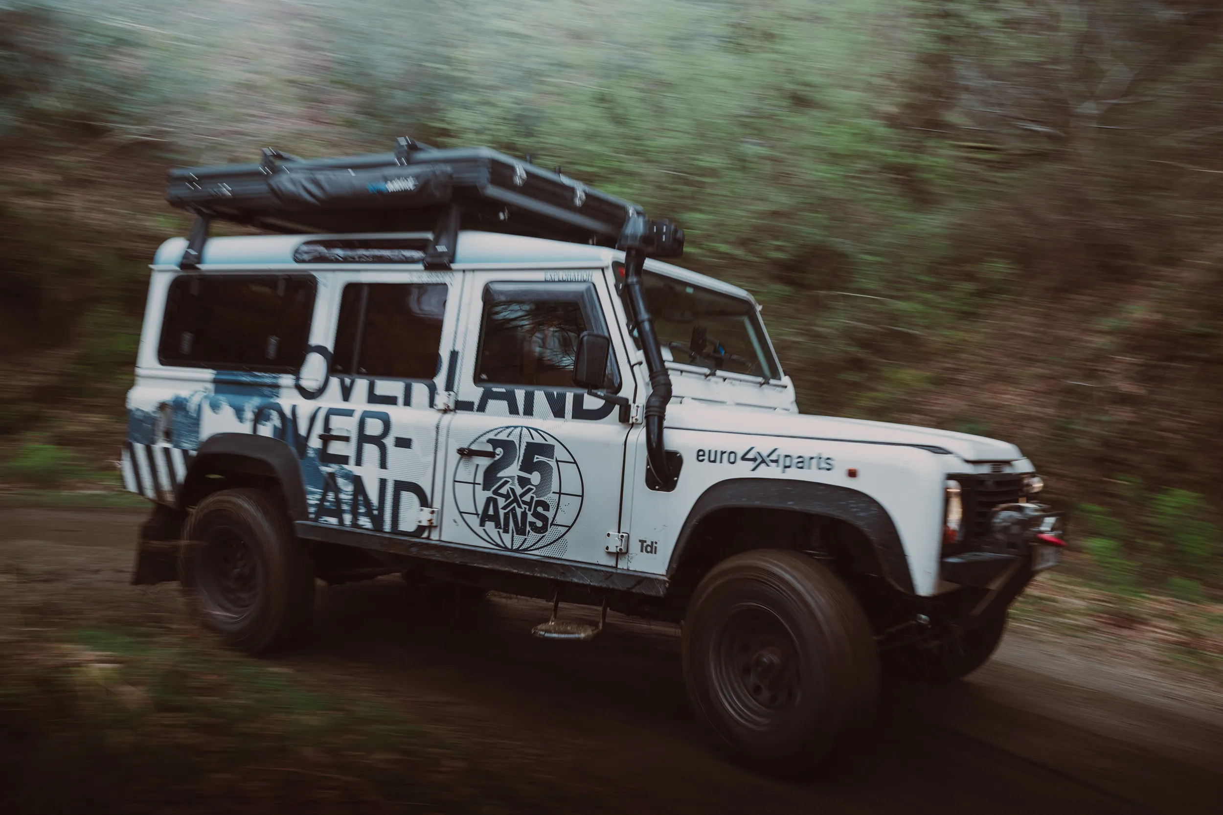 Land Rover Defender blanc « Overland » d'Euro4x4Parts en mouvement sur une piste forestière