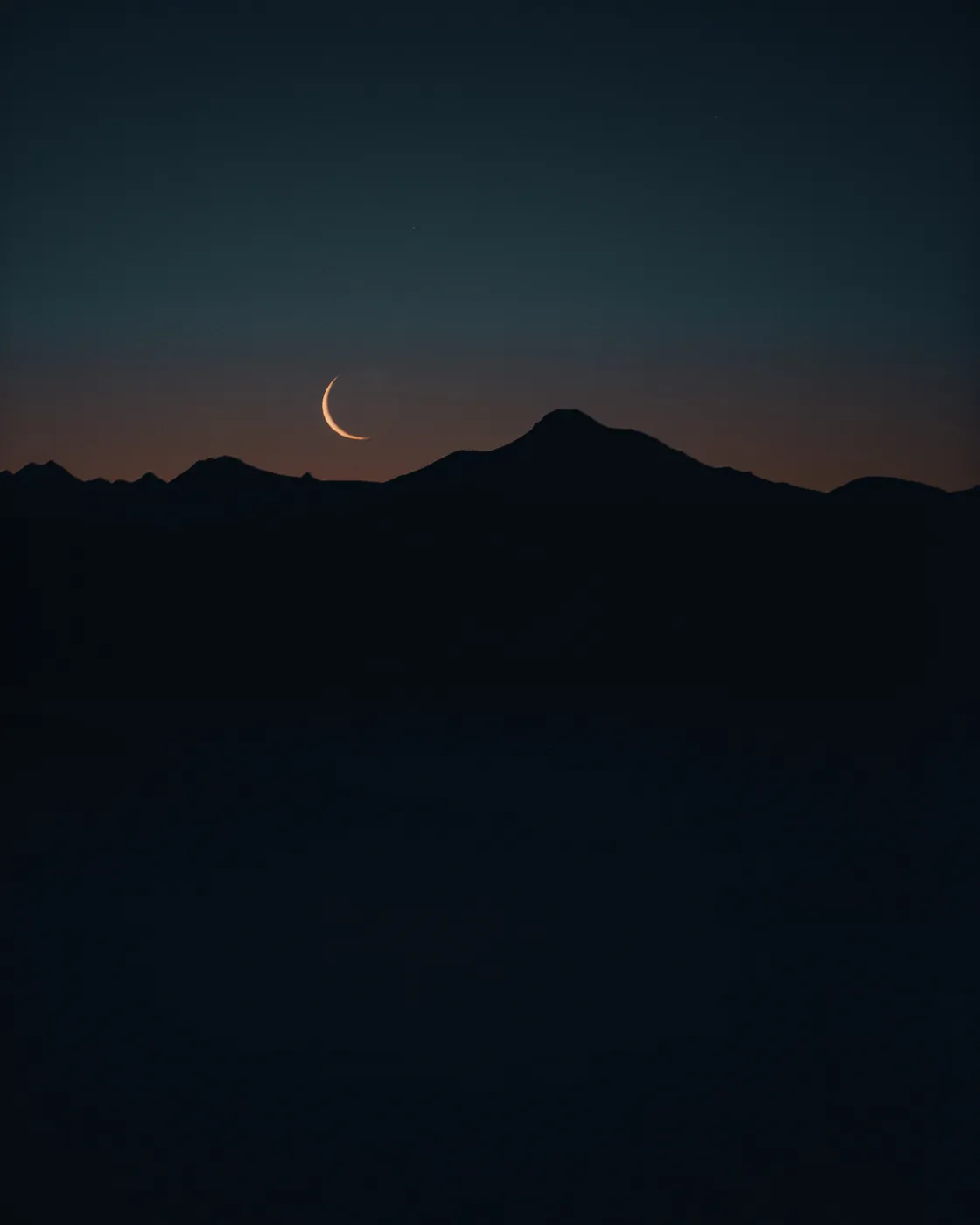 Un fin croissant de lune se couche derrière la silhouette des montagnes, depuis la crête d'Iparla
