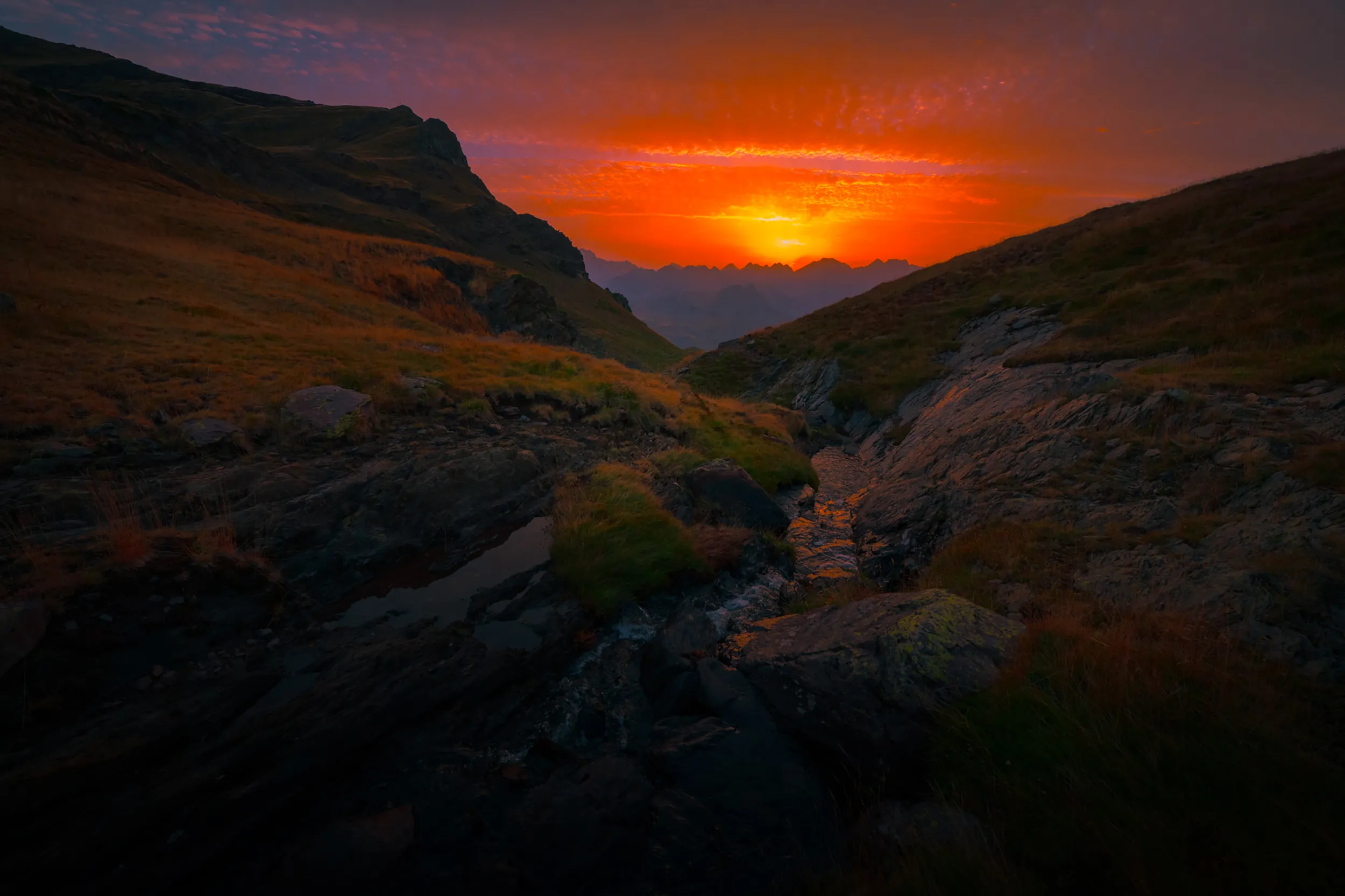 Le soleil se couche entre deux versants herbeux du massif d'Anayet, au-dessus d'un vallon rocheux