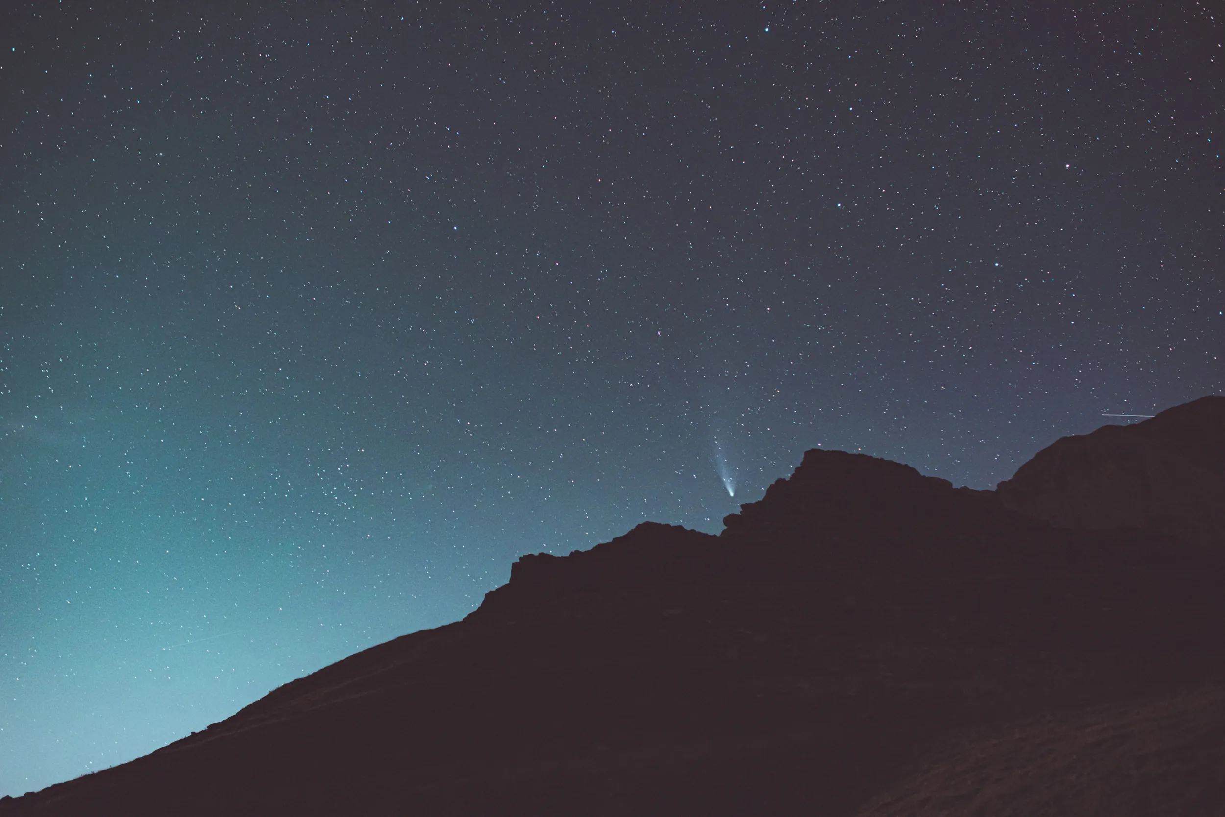 La comète NEOWISE et sa queue au-dessus d'une crête pyrénéenne, dans le ciel bleu de la nuit