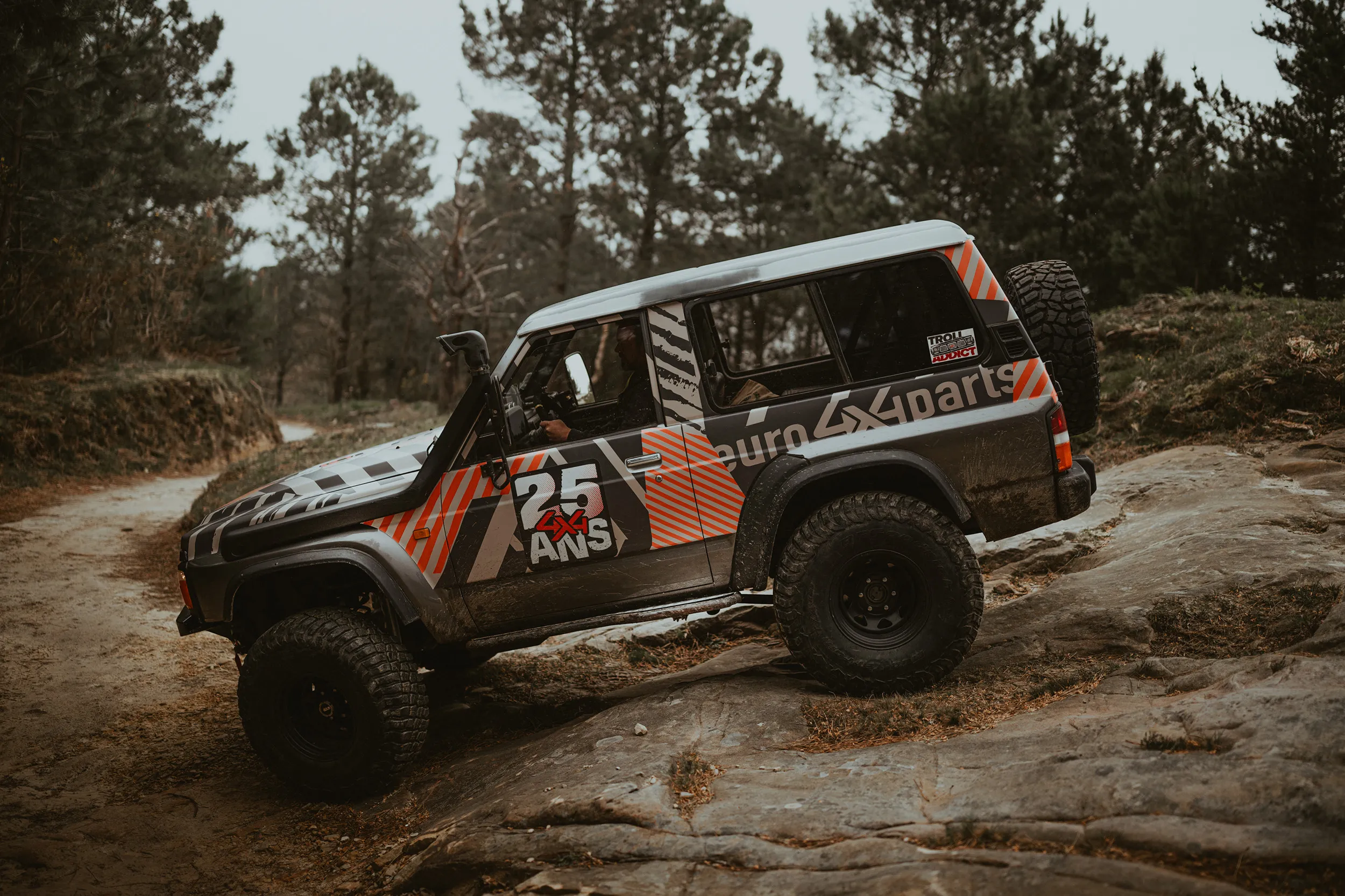 Nissan Patrol aux couleurs des 25 ans d'Euro4x4Parts en franchissement sur un rocher, en forêt de pins