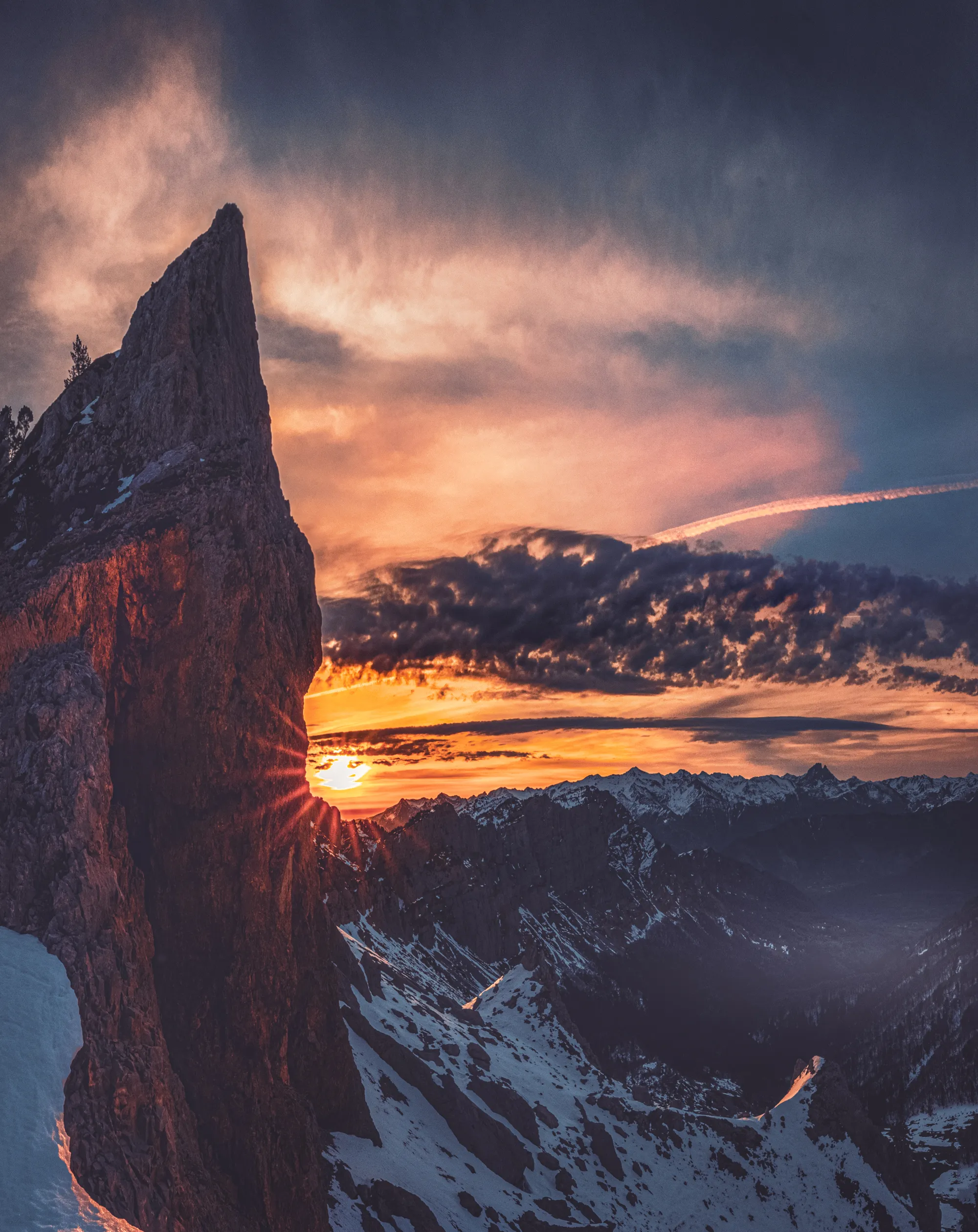 Une aiguille rocheuse se découpe sur un soleil couchant au-dessus des sommets enneigés, au Pas d'Azun
