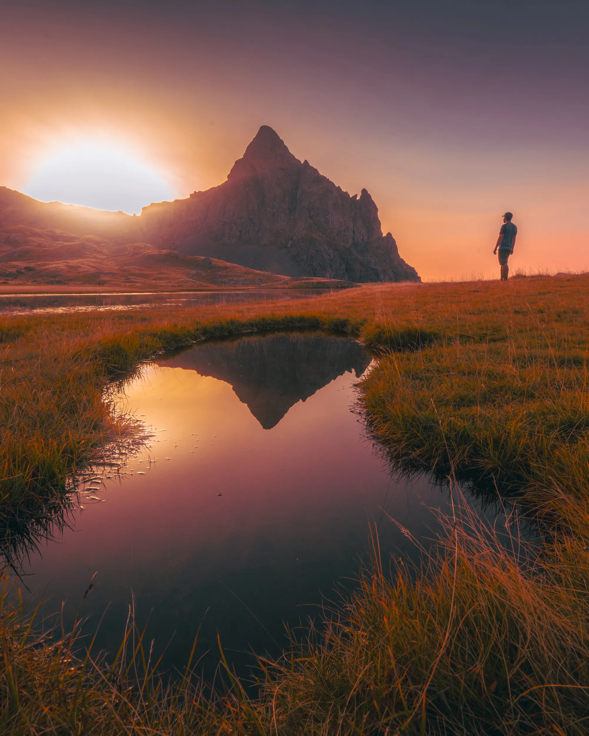 Un randonneur contemple le pic d'Anayet qui se reflète dans une mare d'altitude au coucher du soleil