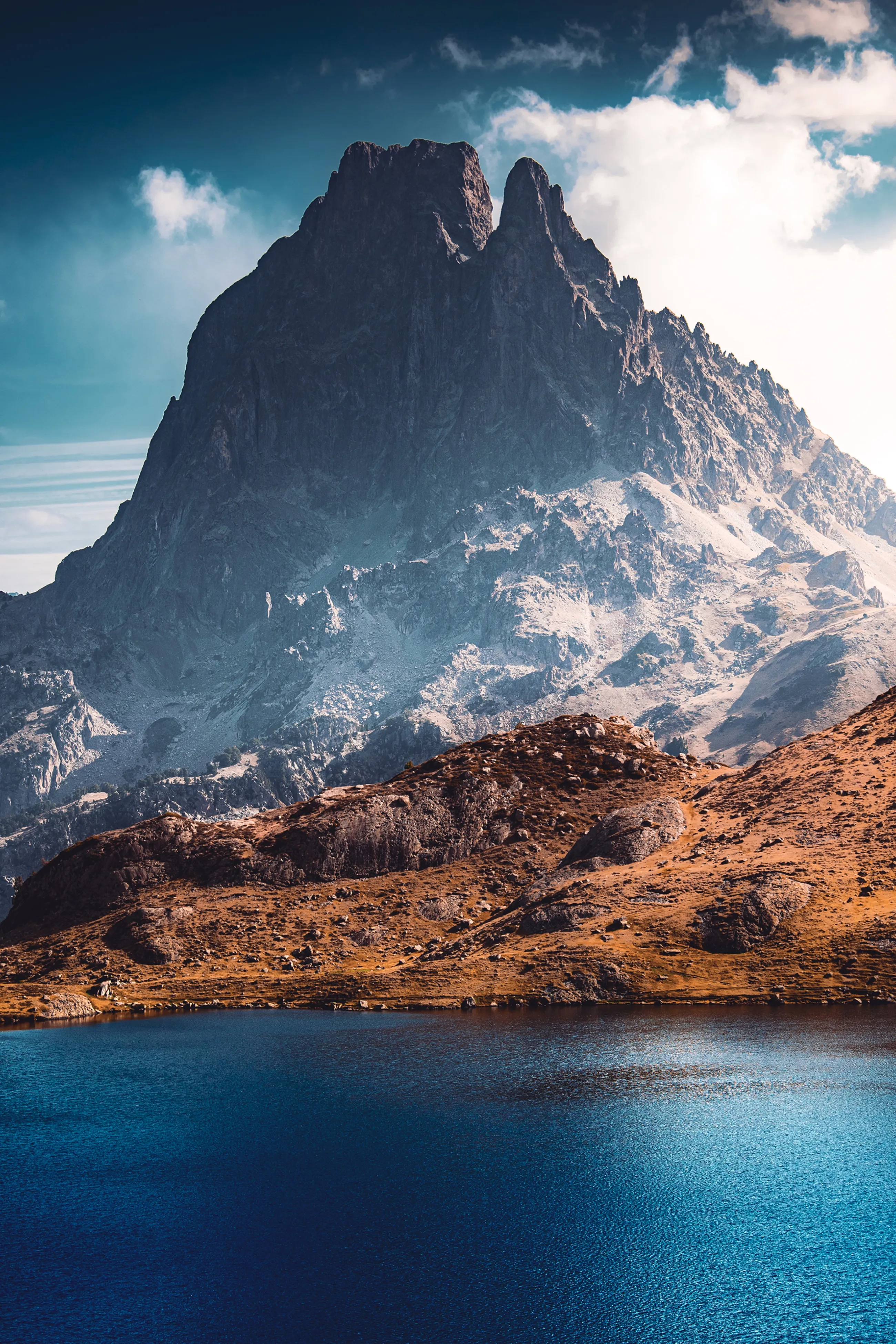 Le pic du Midi d'Ossau et sa double dent, saupoudrés de neige, au-dessus d'un lac d'altitude bleu profond