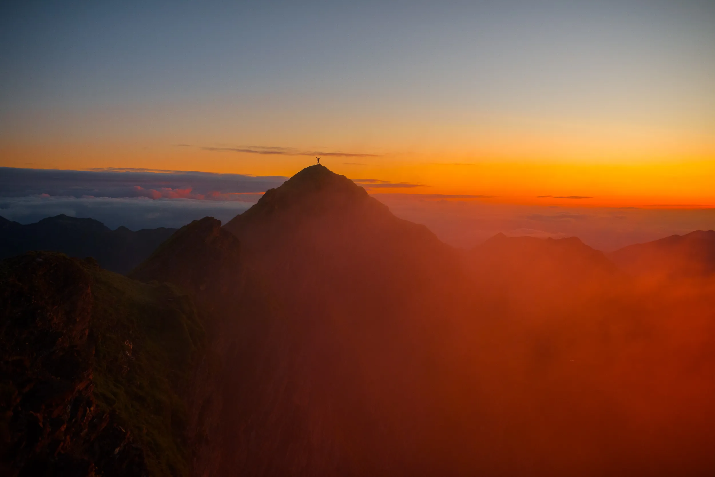 Une silhouette au sommet du pic du Montagnon d'Iseye, dans la brume orangée du soleil couchant