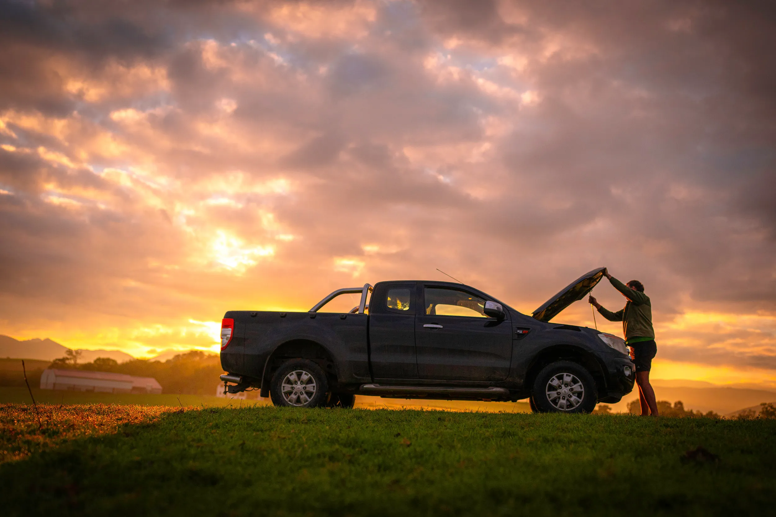 Pick-up capot ouvert dans un pré au coucher du soleil