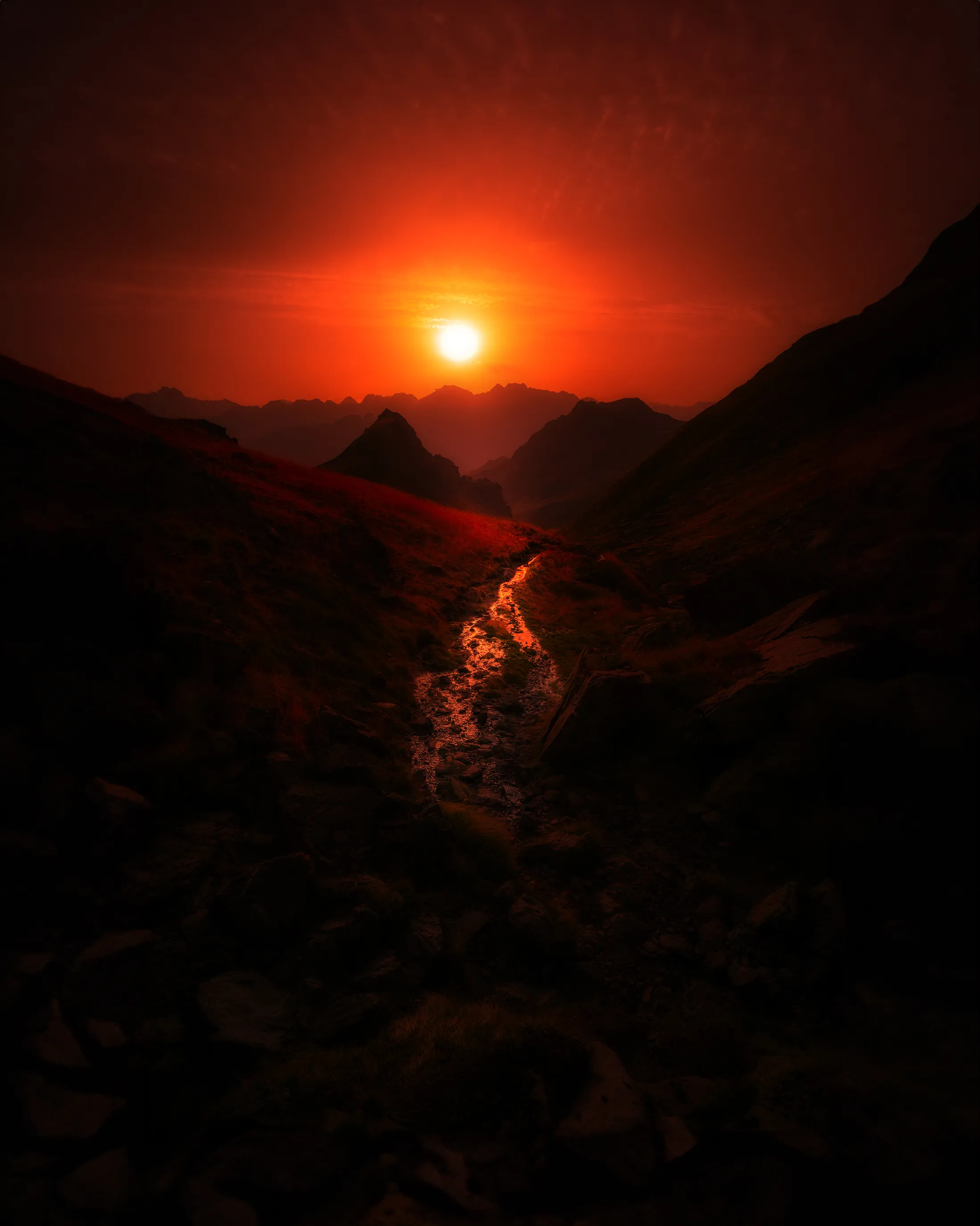 Un soleil rouge vif se couche au fond d'une vallée pyrénéenne et embrase le torrent