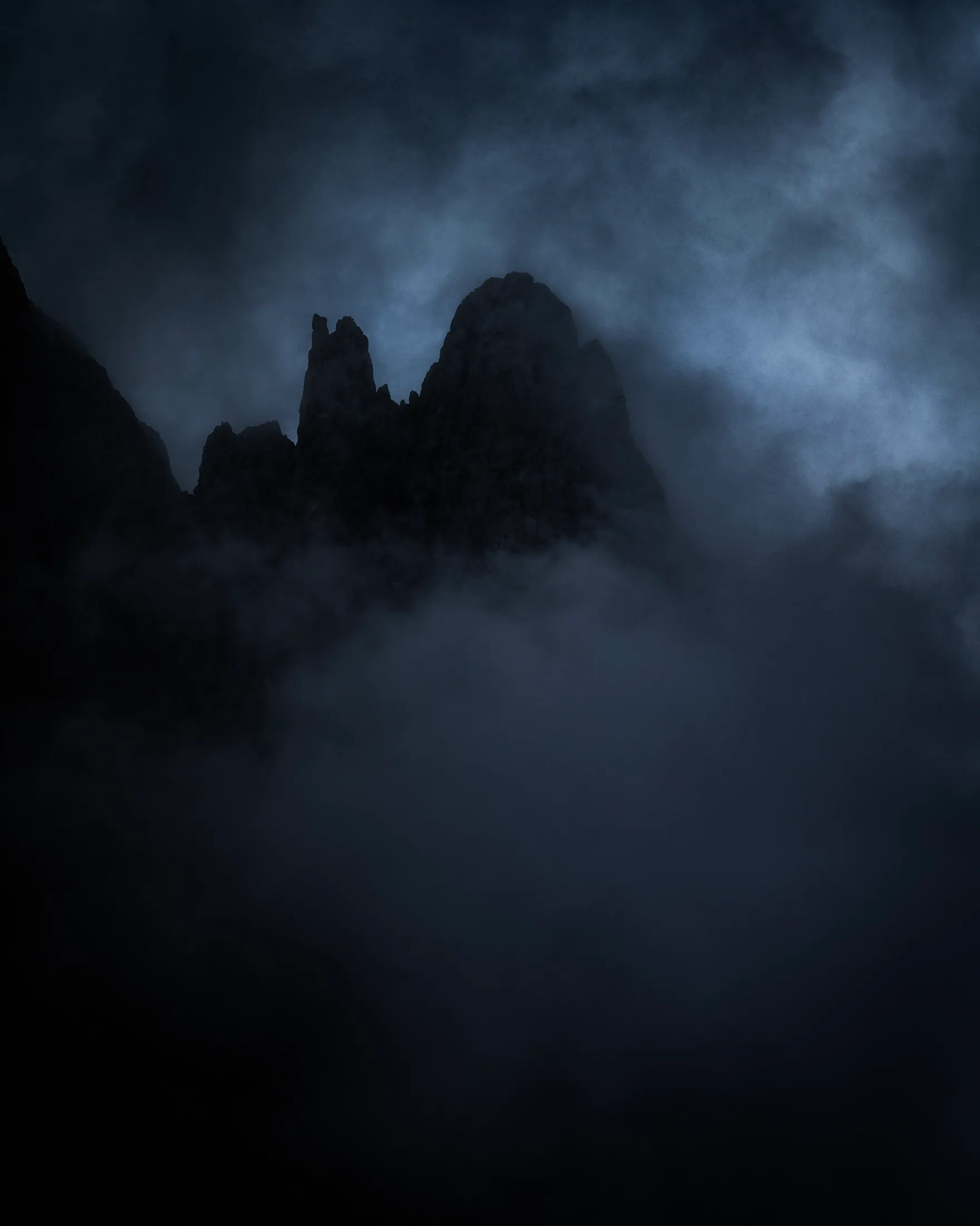 Des tours rocheuses surgissent des nuages et de la brume dans une atmosphère sombre et mystérieuse