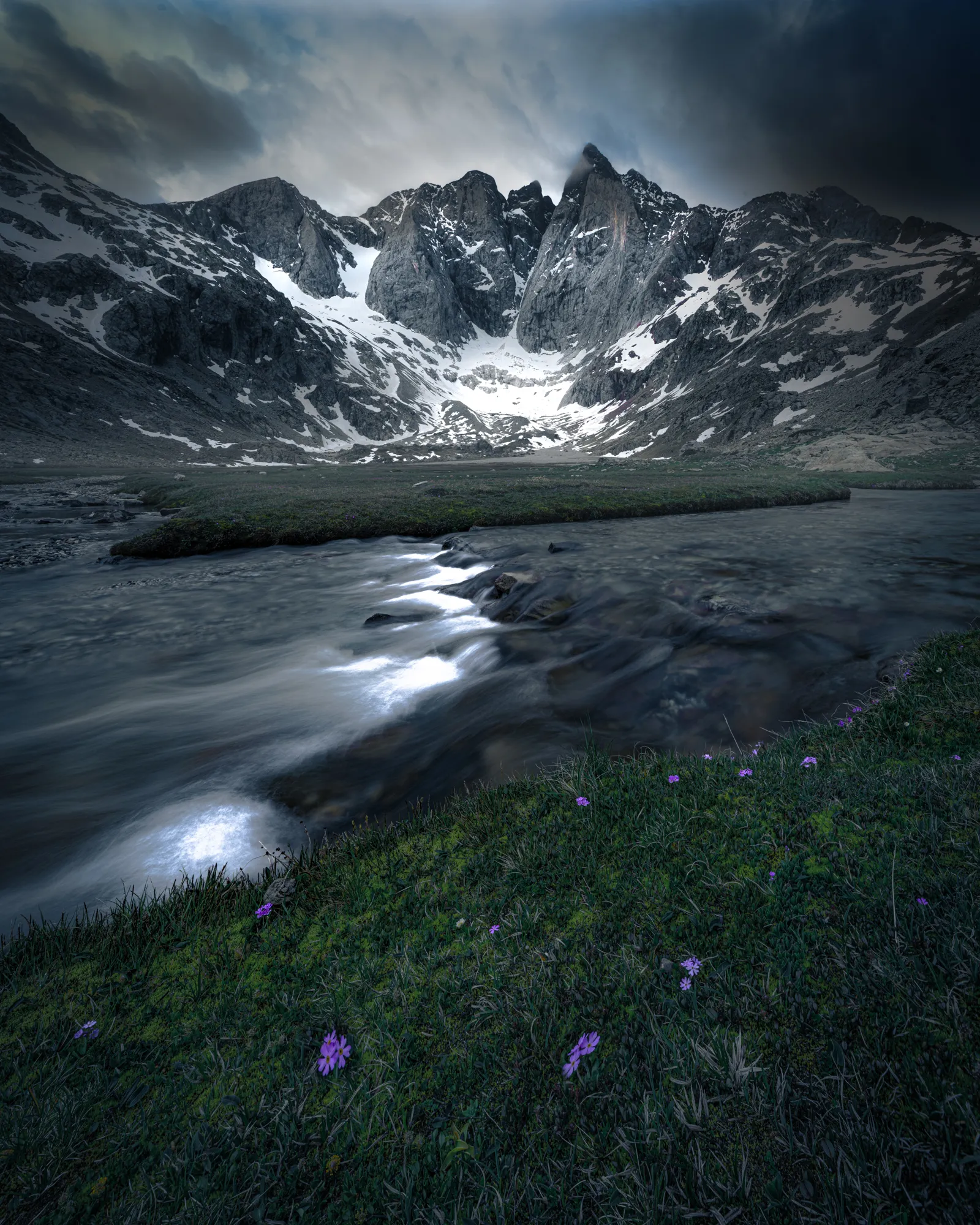 La face nord du Vignemale et son glacier sous un ciel d'orage, au-dessus d'un torrent bordé de crocus
